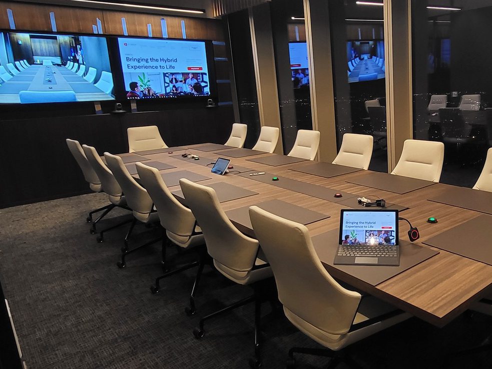 Top-AV-Solutions-for-2025-1 Professional conference room with a sleek rectangular table, surrounded by ergonomic office chairs. The space includes neutral-toned walls, subtle lighting fixtures, and minimalistic decor, creating a clean and modern atmosphere suitable for business meetings or presentations.
